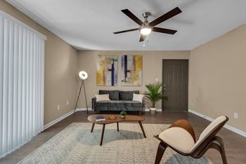A living room with a grey couch, a brown chair, and a ceiling fan at Crystal Lake in Pensacola, Florida.
